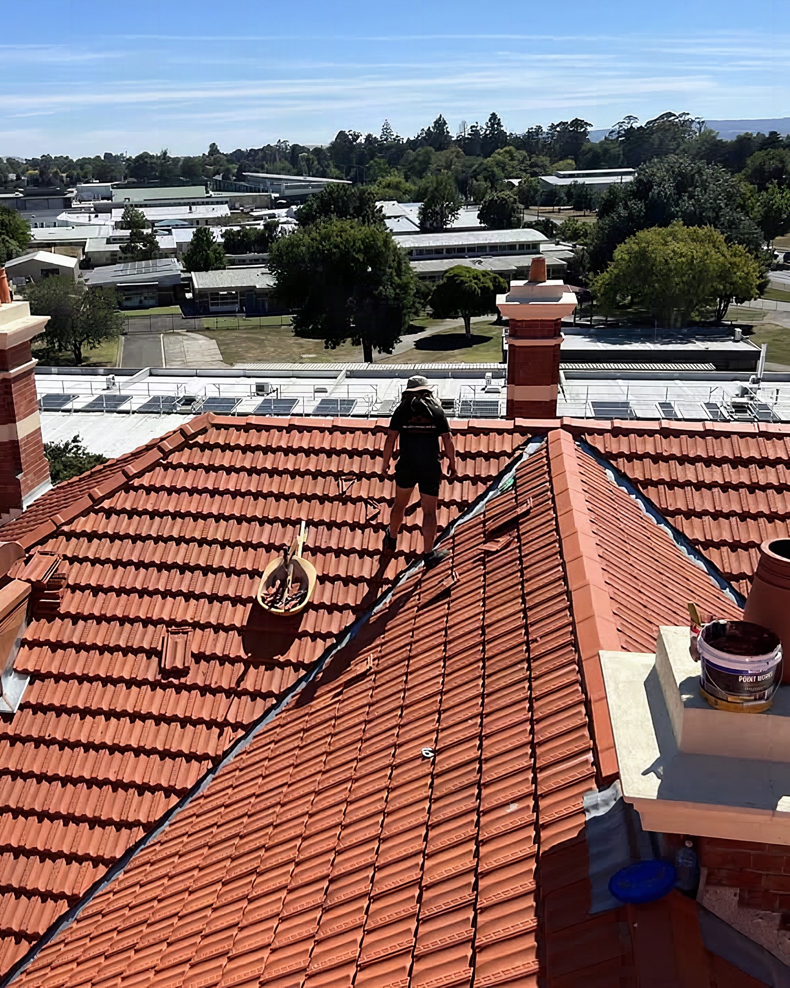 A roofer walking the ridge of a large terracotta tile roof above Ballarat