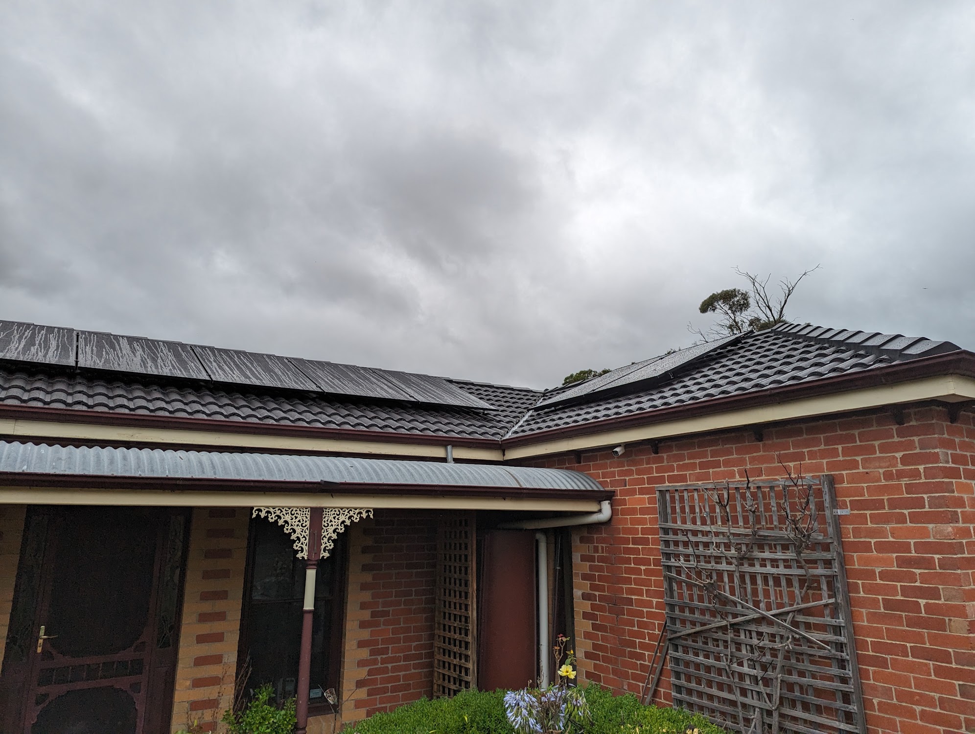 A brick home with a newly laid dark tile roof under heavy cloud