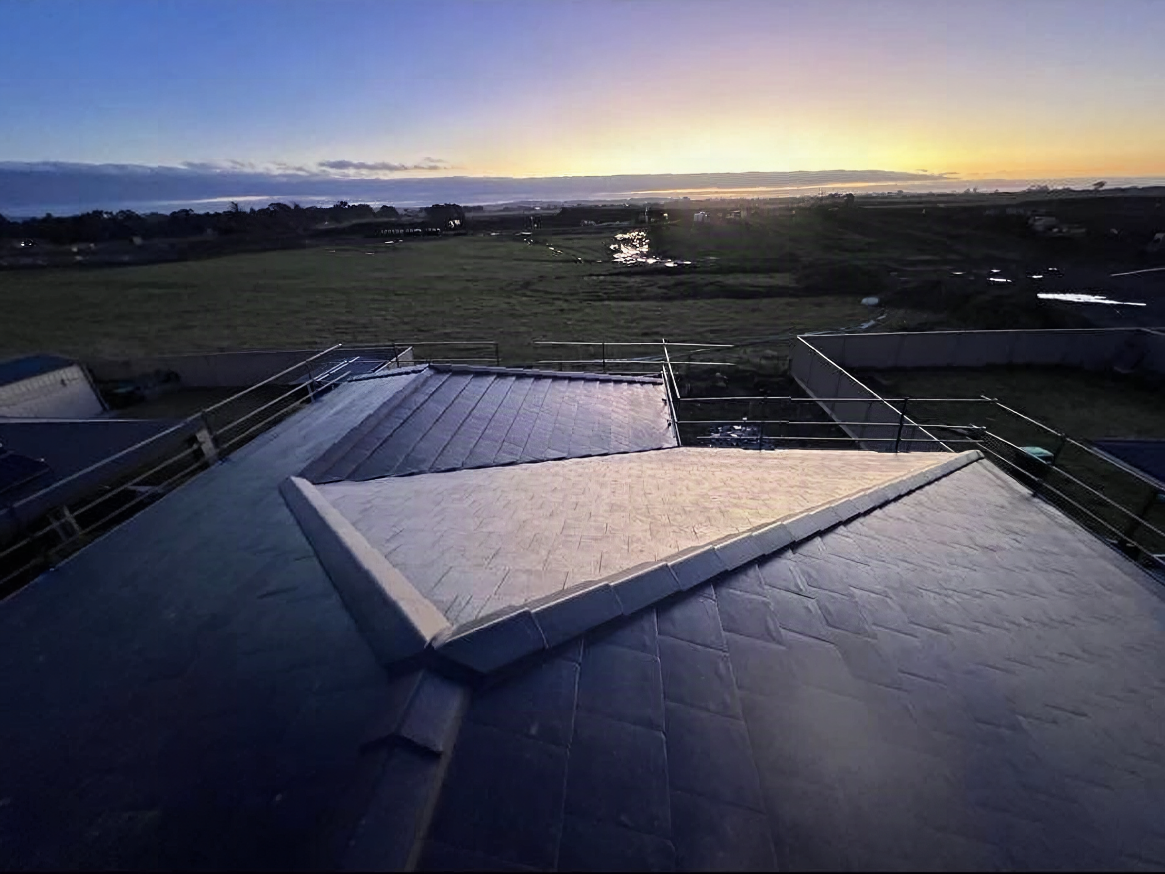 Dawn light over a low roof and the paddocks beyond it