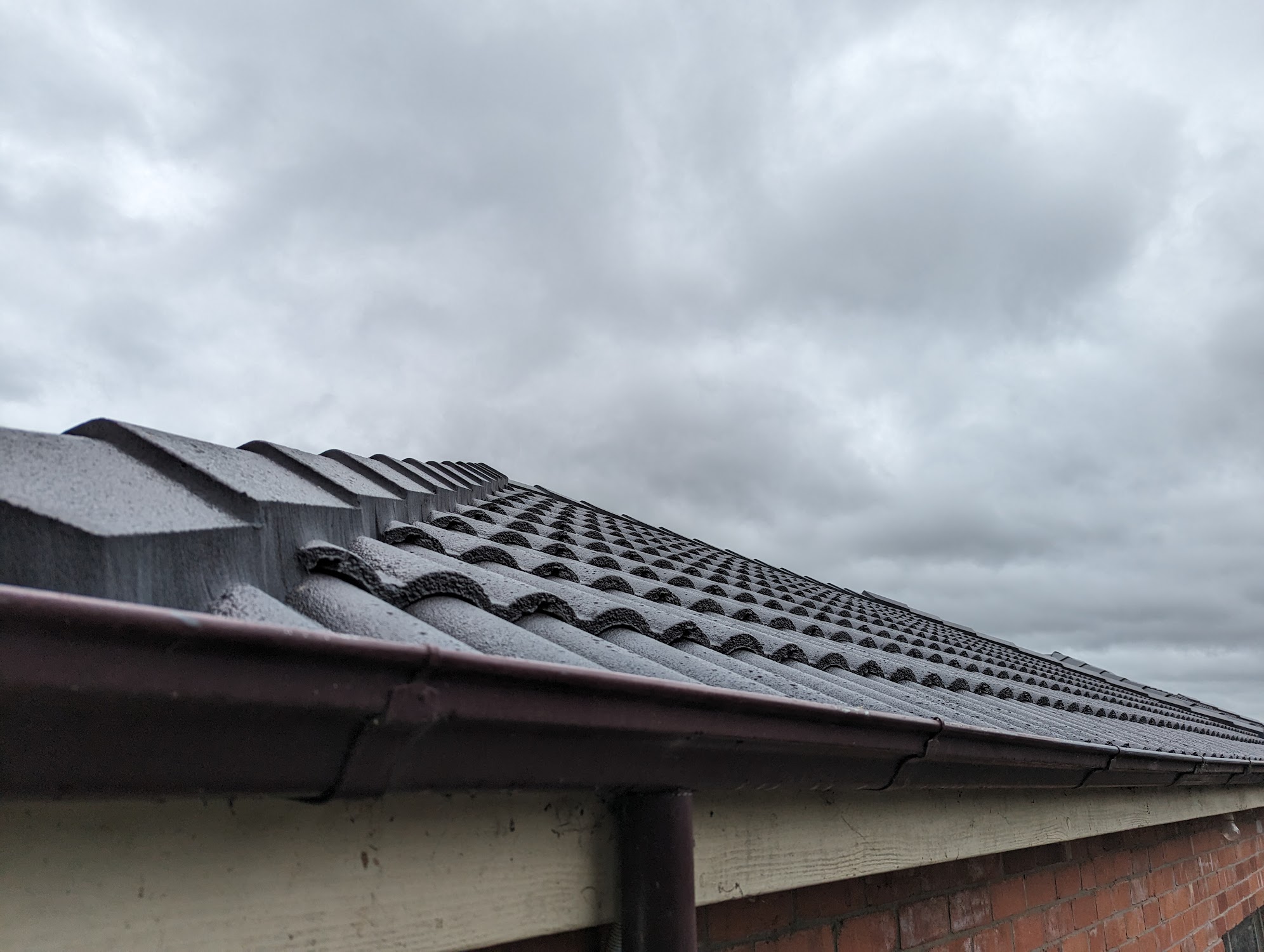 The edge of a newly laid dark tile roof and its gutter line under a grey sky