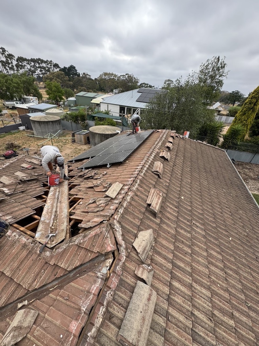 A roofer lifting old tiles from a section of roof mid-repair