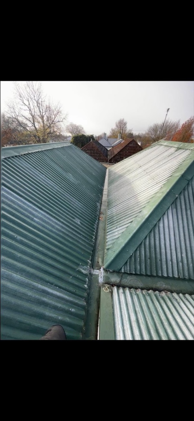 A wide metal box gutter running between two corrugated roof sections