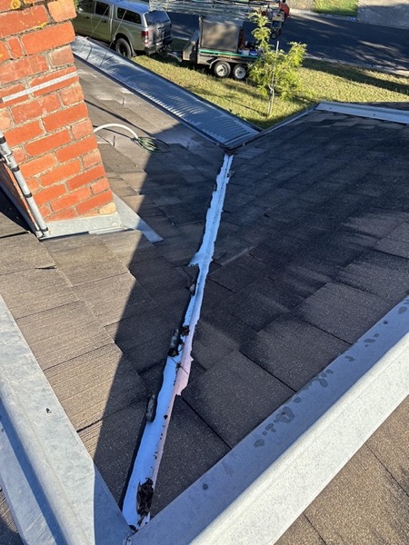 A new metal valley running between two roof planes beside a brick wall