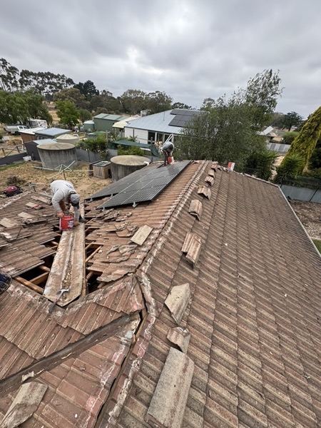 A roofer lifting old tiles from a section of roof mid-repair