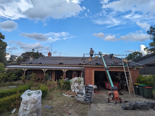 A roofer working along the ridge of a brick home with a ladder against the gutter