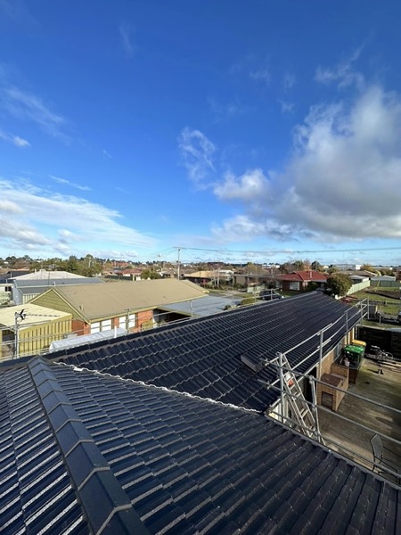 A dark tile roof against blue sky with neighbouring homes behind