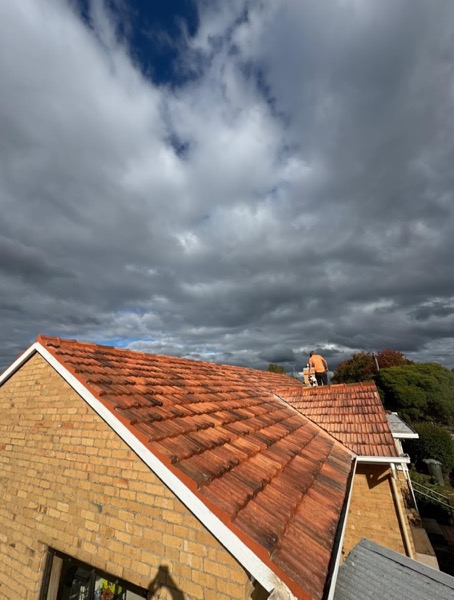 A terracotta tile roof under cloud with work under way along the ridge