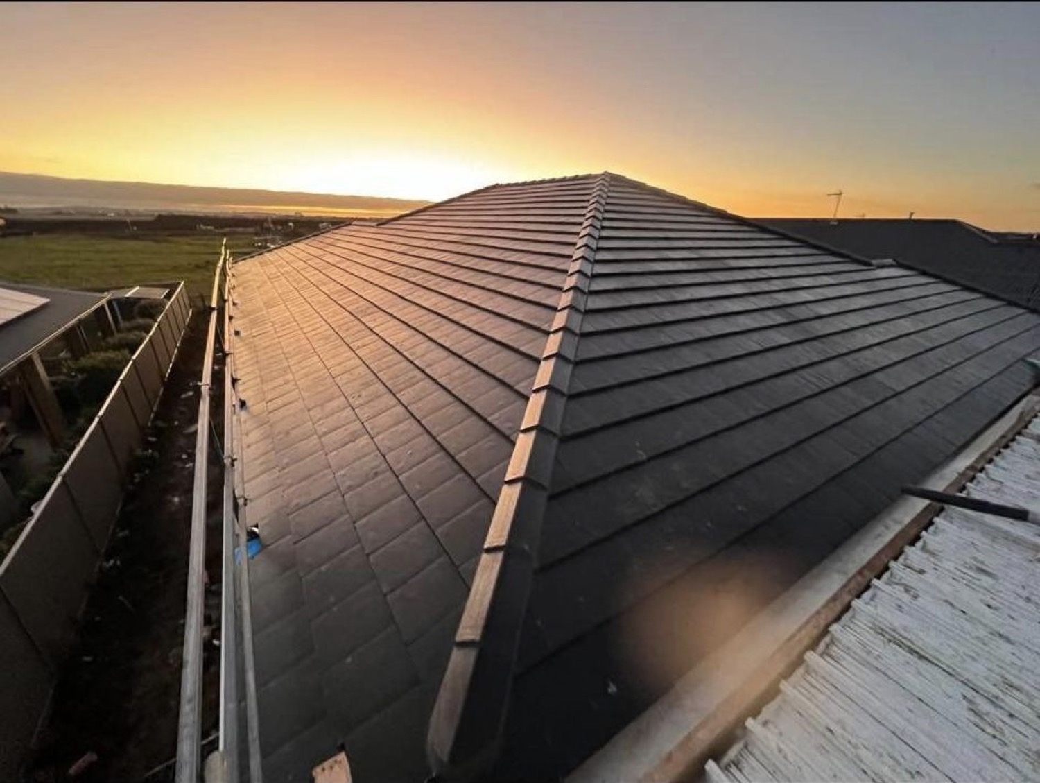 A newly tiled hip roof catching first light over open country